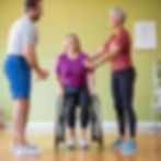 Group of sci clients standing up with a partner. partner has hips
and gait belt around clients knees to assist in standing exercises.
Casual, active atmosphere with blurred figures in motion.
.