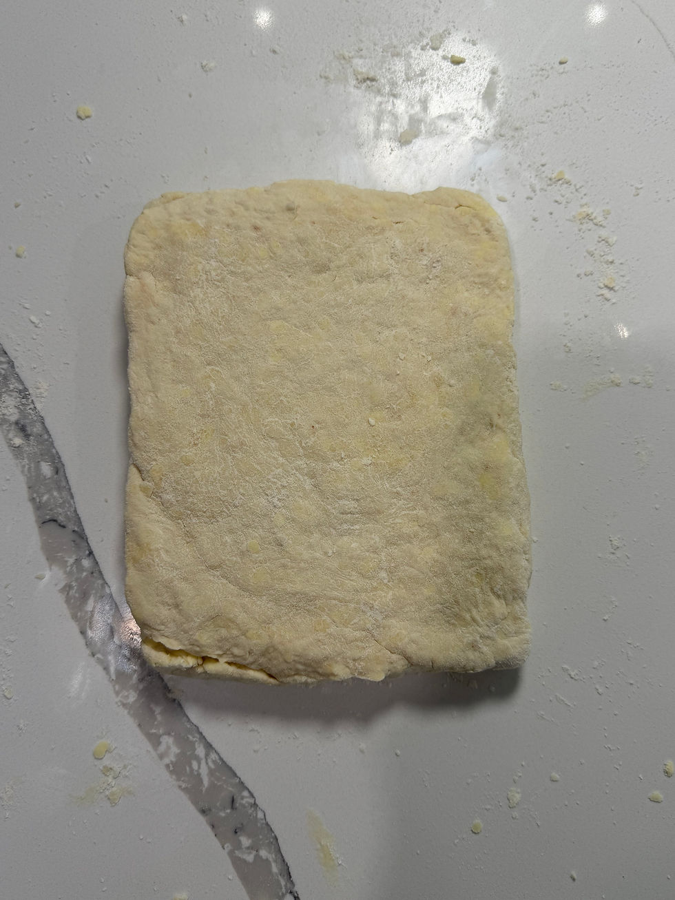 Square block of pale dough on a floured white countertop, with flour dust and smears around it.