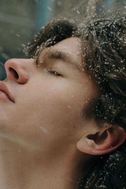Extreme close-up of young man's face with eyes closed and snowflakes on his eyelashes, NYC snow day editorial portrait