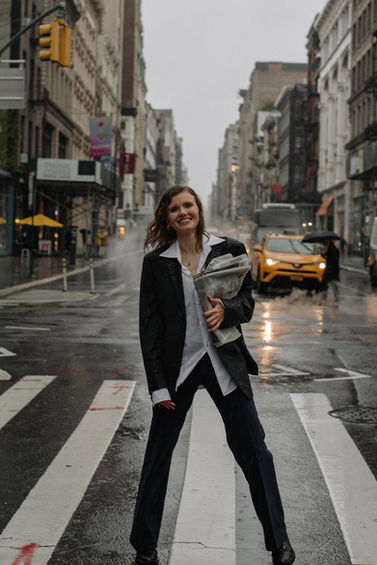 Color street portrait of a woman in a black blazer posing on a rain-soaked SoHo crosswalk with yellow taxi behind her, NYC