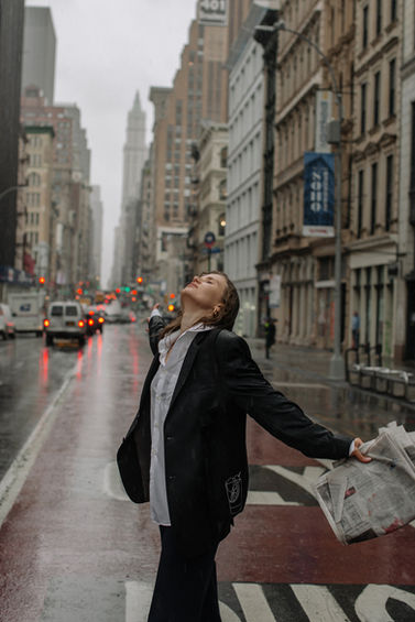 Black and white street portrait of a woman in a black blazer with her head tilted back in the rain on a SoHo crosswalk, NYC