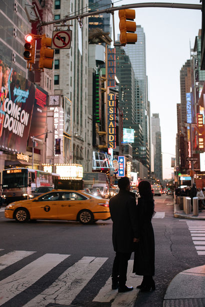 Silhouette of couple on a Times Square crosswalk at night, yellow cabs and glowing billboards and neon signs behind them, NYC