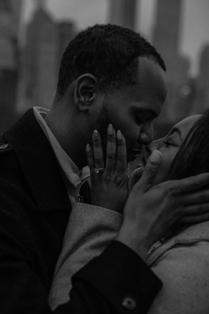 Black-and-white close-up of couple kissing, engagement ring pressed against his face, Central Park NYC proposal portrait