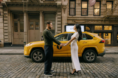 Couple holding hands on SoHo cobblestone street beside a yellow cab, Charles Bro storefront behind them, NYC