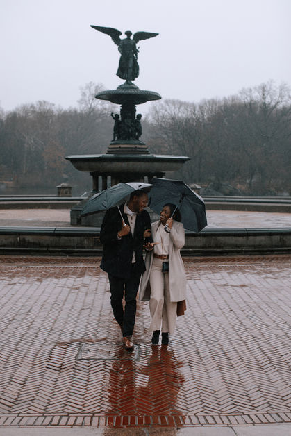 Just-engaged couple with umbrella in front of the Angel of the Waters fountain at Bethesda in Central Park on a rainy day, NYC