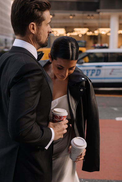 Candid shot of couple on a Midtown street, bride holding a coffee cup, NYPD car and yellow cab in background