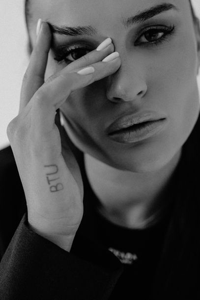 Black and white studio close-up portrait of a woman with hand near face revealing an arm tattoo, NYC