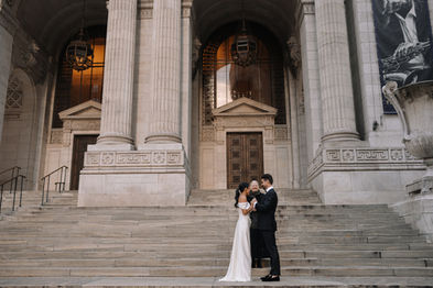 Wide shot of couple kissing on the grand steps of the New York Public Library, stone columns and arched entrance behind them
