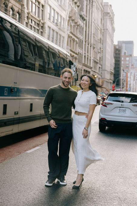 Couple walking together past a bus on a SoHo street, cast-iron buildings and yellow cabs behind them, NYC