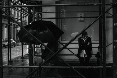 Black and white editorial portrait of a woman in a black outfit with umbrella under rain-soaked SoHo construction scaffolding, NYC