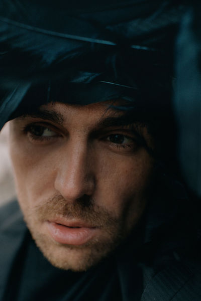 Extreme close-up of man's face partially covered by black feathers, dark moody light, NYC conceptual editorial portrait