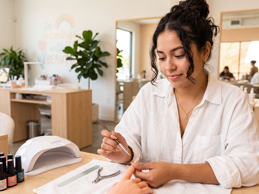 Mujer haciendo manicura en un salón luminoso, con esmaltes y lámpara UV, concentrada y en ambiente tranquilo.