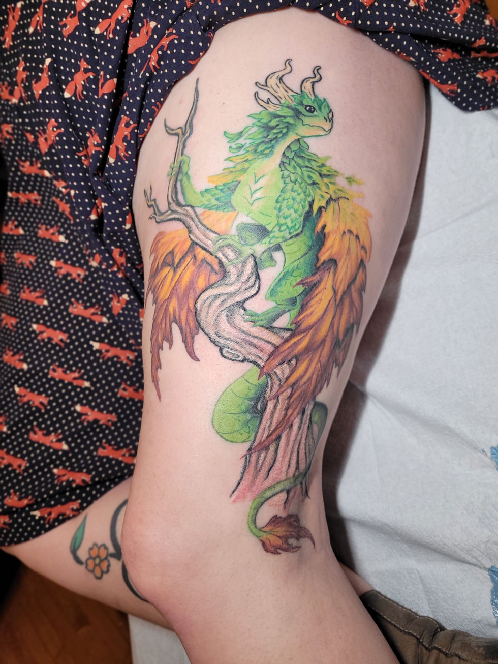 a woman has a tattoo of a green dragon on her leg