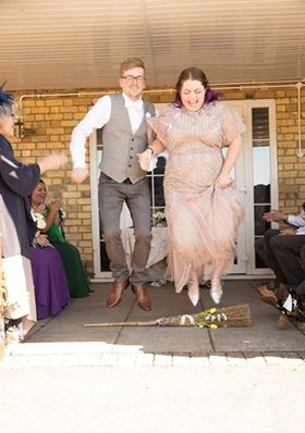 Couple jumping the broom after their celebration ceremony at the local community hall