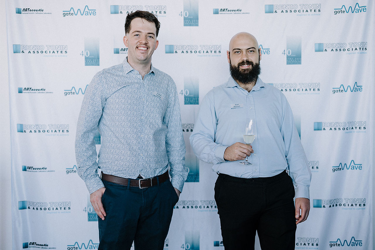2 men in business attire standing in front of a banner