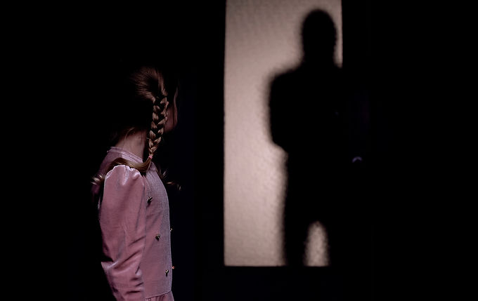 A little girl in PJs gazing at an ominous silhouette on her bedroom wall.