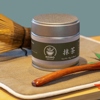 Matcha powder with whisk and wooden spoon, Momo Matcha product on display.