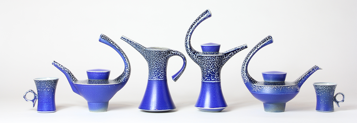 A row of six cobalt blue drinking vesserls, teapots and objects with a small abstract pattern, on a white background.