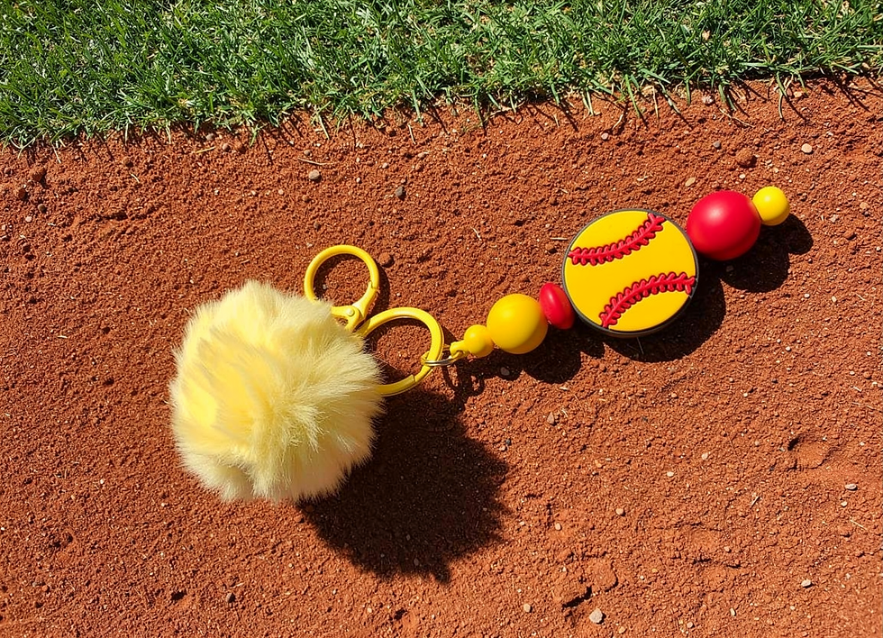 Thumbnail: Yellow pom pom softball keychain on dirt field
