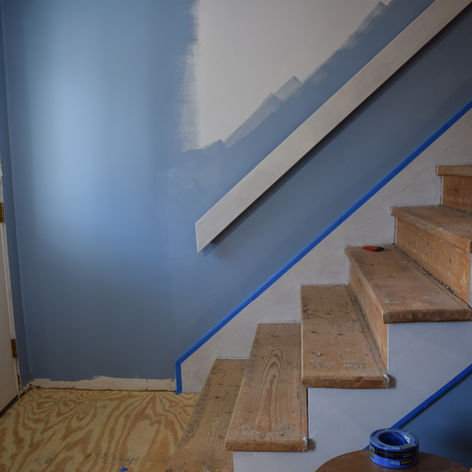 A progress photo of a renovation project depicting a home's stairs stripped to bare wood and walls partially painted