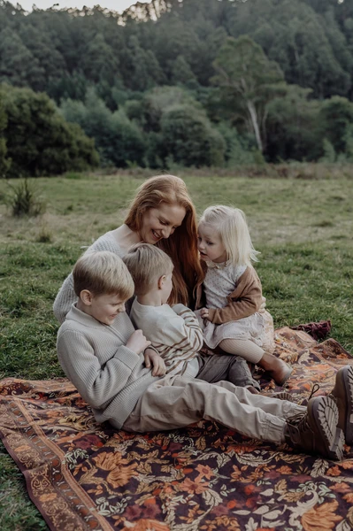 A mother with her three young children, snuggled up on a picnic rug. She's tickling them and they're all laughing and squirming.