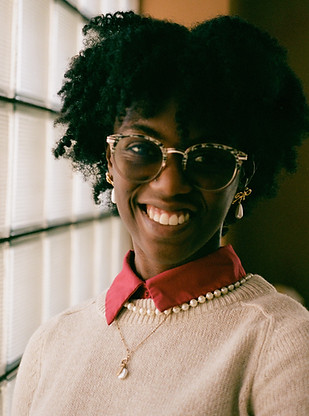 A photo of a young black woman wearing glasses with her hair styled in an afro smiling