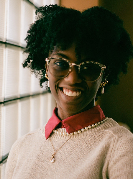 A photo of a young black woman wearing glasses with her hair styled in an afro smiling