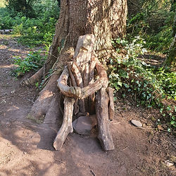 Wooden sculpture of a sitting figure at a tree base.