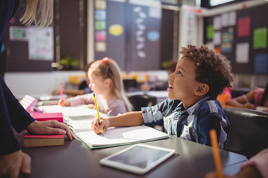 A young student looks up while writing at their desk.