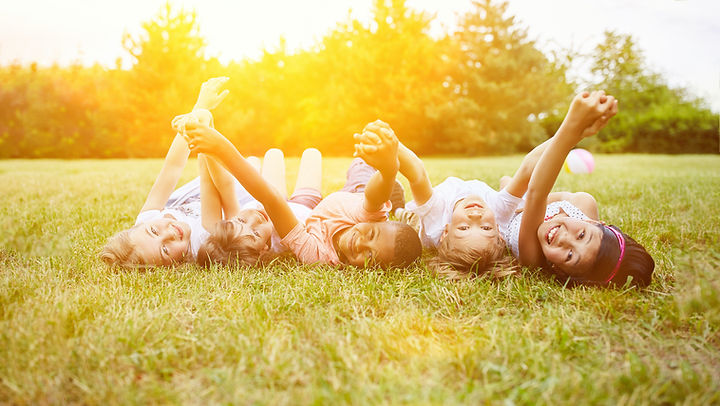 A group of children lay on their backs, holding their hands up in the air and looking at the camera smiling.
