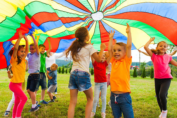 Young children play under a rainbow parachute.