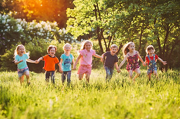 A group of young children hold hands while running on grass.