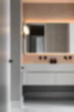 Modern bathroom with grey walls, marble floor, and white vanity. Black fixtures, soft lighting, and round wall light create a sleek ambiance.