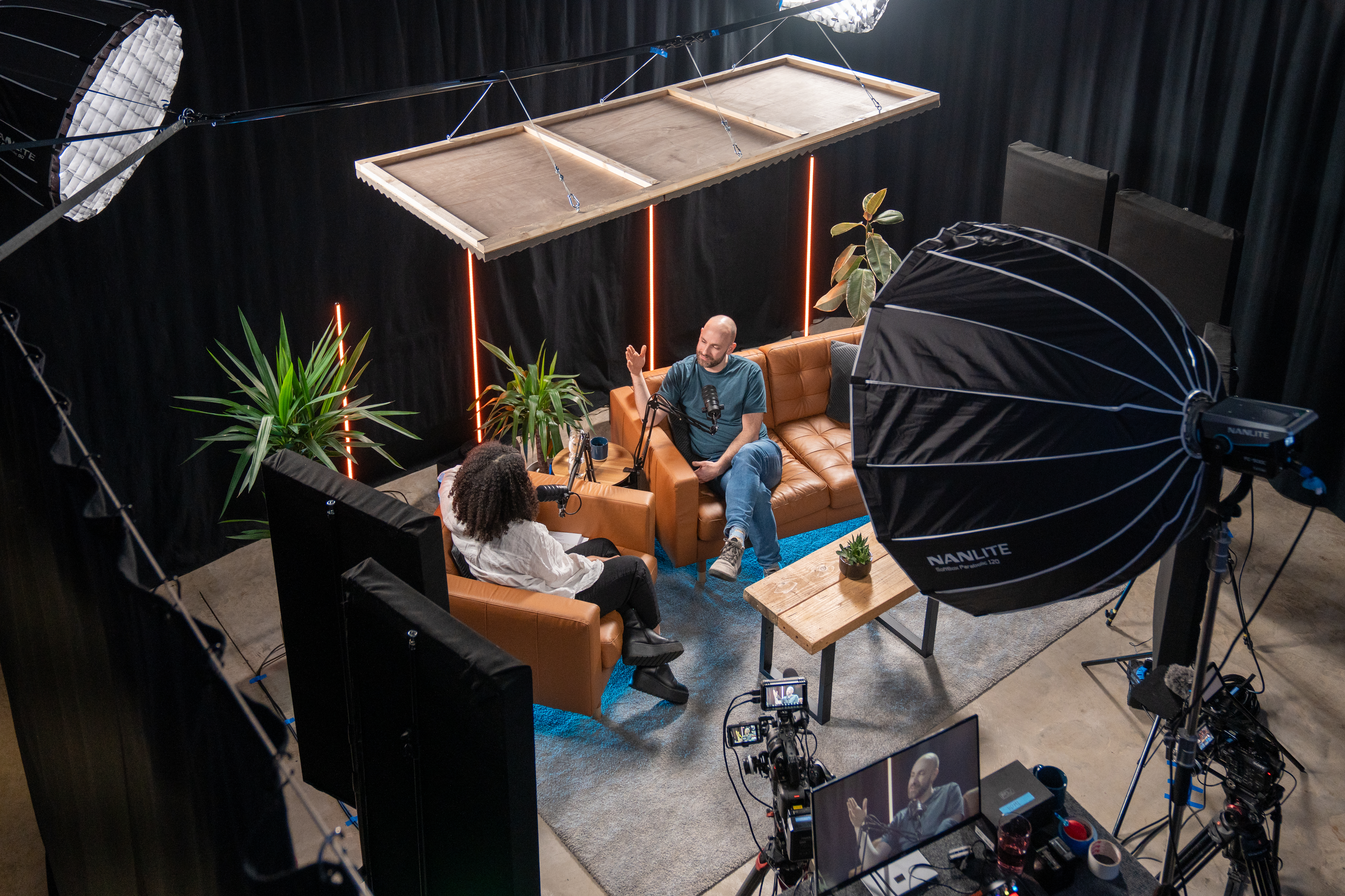 A two-person video podcast shoot at Speed Motion Studios with cameras, lights, microphones and a dressed sofa set.