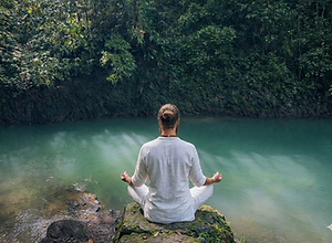 Personne méditant en silence, assise sur un rocher au bord d'une rivière turquoise dans la jungle