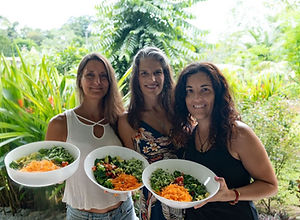 Trois femmes souriantes tenant des bols de salades fraîches et colorées dans un jardin tropical, lors d'une retraite à Arbol Essence au Costa Rica