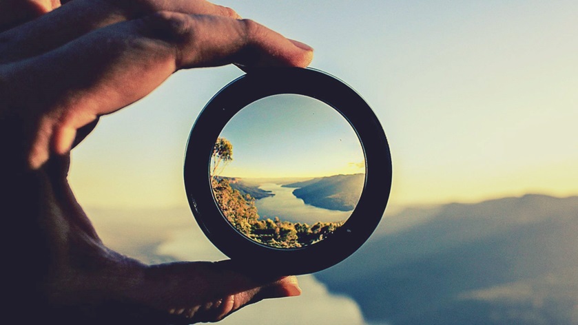 Hand holding a lens, focused on a lake and mountains