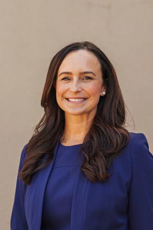 Smiling female team member with long brown hair in a blue blazer.