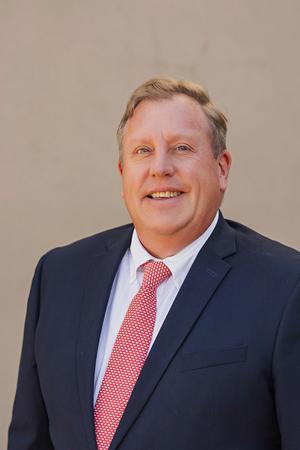 Smiling man in a navy suit and pink tie.