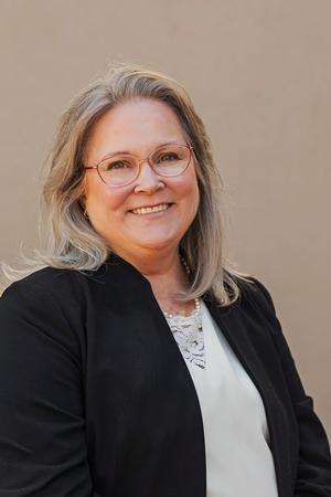 Smiling female team member with glasses and a black blazer.