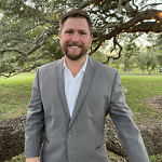 Smiling team member in a grey suit outdoors.