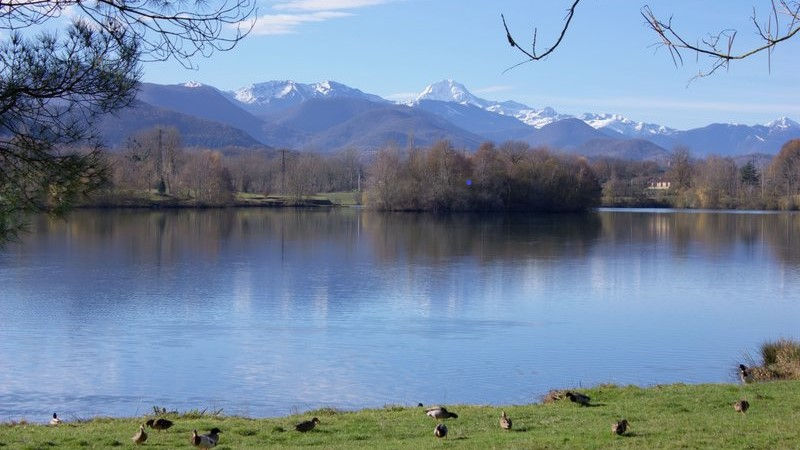 Vue du lac de Montréjeau avec les sommets des Pyrénées en arrière-plan. Ce site emblématique du Comminges est particulièrement apprécié durant les journées de fortes chaleurs pour sa plage, ses espaces de détente et ses activités de plein air.