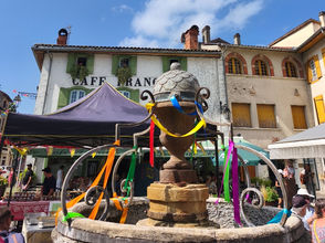 La fontaine du centre d'Aspet entourée des étals et des visiteurs lors du marché hebdomadaire au cœur du village.