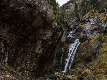 Cascade naturelle au cœur des Pyrénées entourée de falaises et de forêt.