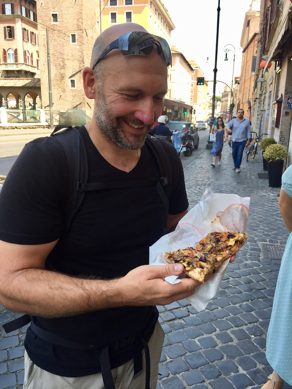 Man smiles ready to eat slice of pizza on a Rome street