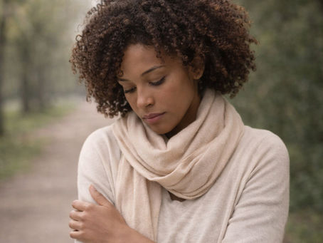 Woman walking along a tree-lined path holding herself in a pause from anxious overthinking.