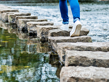 A person walking carefully across stepping stones in a shallow river, symbolising gradual progress, balance and moving forward one step at a time in SEND education.