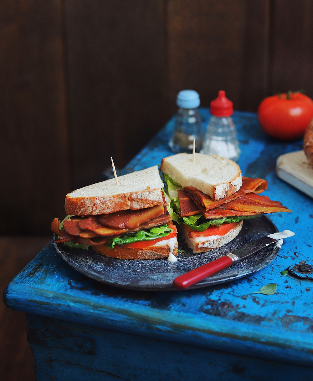 vegan bacon sandwich on a black plate on a blue worktop