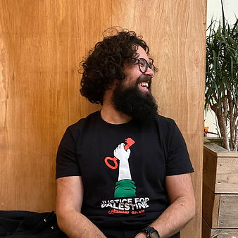 Marcus Bernard, Freelance Producer. Marcus has dark hair, glasses and a beard. He wears a black tshirt with the image of a hand holding a red key. He looks to his left and laughs.