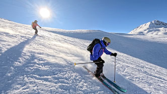two skiers ski touring down ski slope with snow covered mountain in background